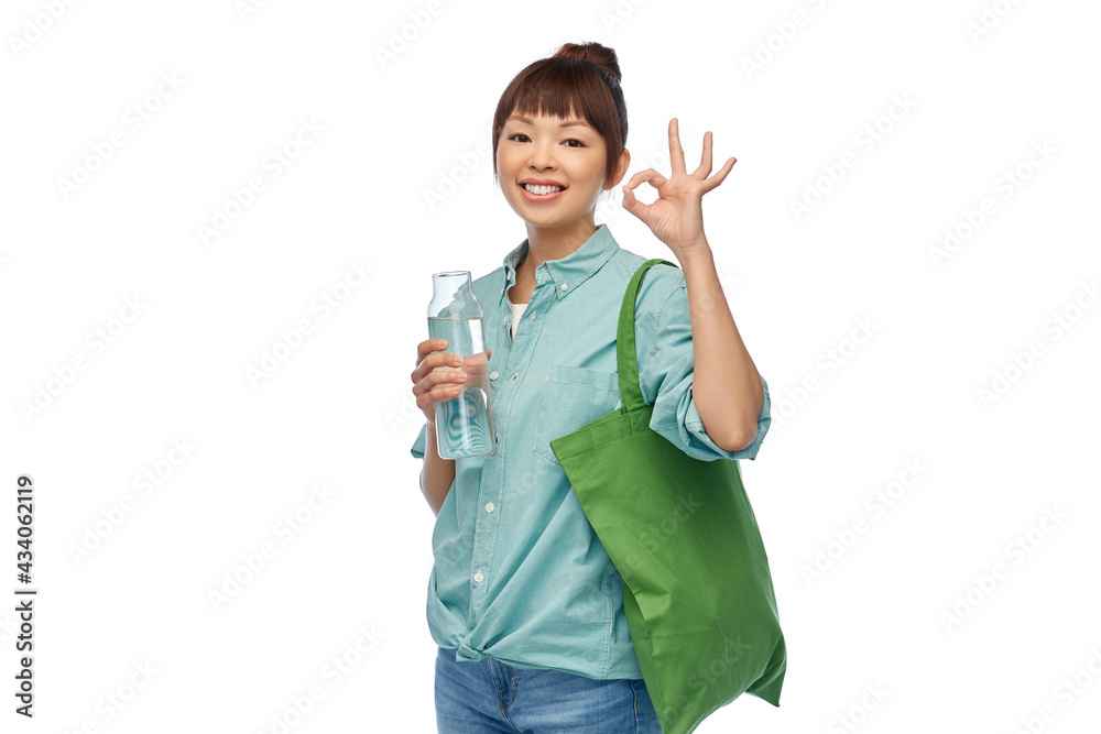 sustainability, eco living and people concept - portrait of happy smiling young asian woman with green reusable bag for food shopping and glass bottle of water showing ok gesture over white background sustainability, eco living and people concept - portrait of happy smiling young asian woman with green reusable bag for food shopping and glass bottle of water showing ok gesture over white background