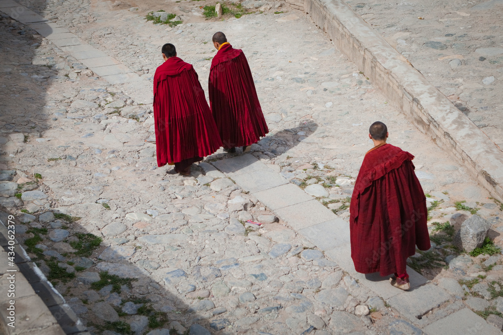 Three Tibetan monks in traditional dress walking in the historic temple of ancient Kumbum monastery, Qinghai Province, China