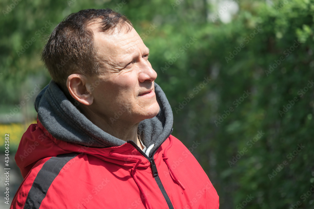 portrait of a mature middle-aged man, handsome, against a background of greenery, looking into the distance portrait of a mature middle-aged man, handsome, against a background of greenery, looking into the distance