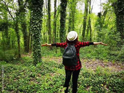 Rear view of a woman with open arms looking at the trees covered with crawling vines in Italy photo