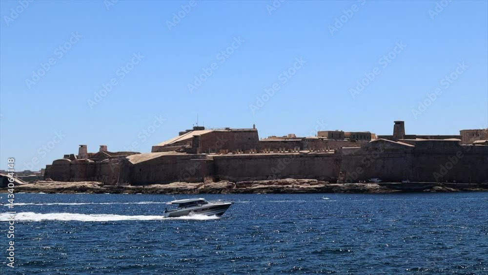 Small luxury motor yacht sailing fast in blue sea with Valletta fortification in background, Slow Motion Small luxury motor yacht sailing fast in blue sea with Valletta fortification in background, Slow Motion
