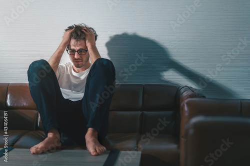 Depressed caucasian man losing job and heartbroken at same time sitting alone on sofa with low light environment, PTSD Mental health and depression concept. photo