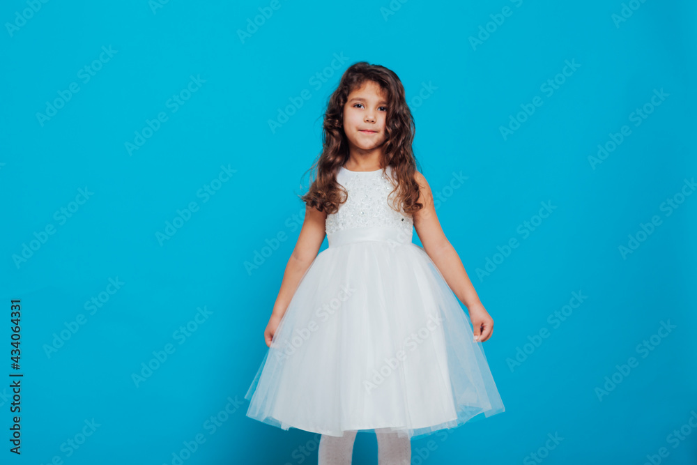 Naklejka premium Beautiful little curly girl 5 years old in a white dress on a blue background