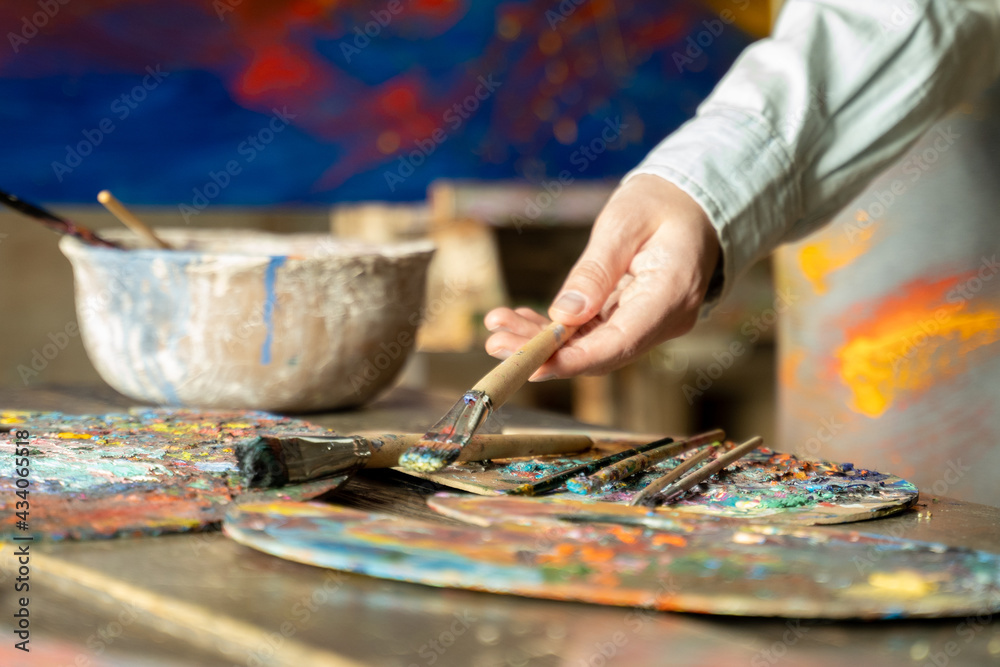 Obraz premium Woman artist hand takes a brush on a painting background. artist creates a painting in the studio