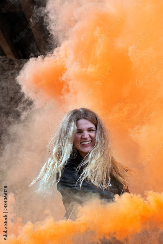 Happy blonde girl on a background of orange colored smoke.