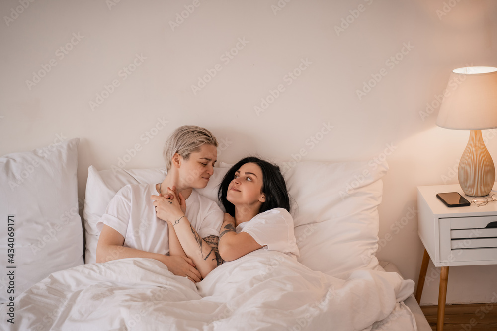 Fototapeta premium smiling lesbian couple lying in bed and holding hands