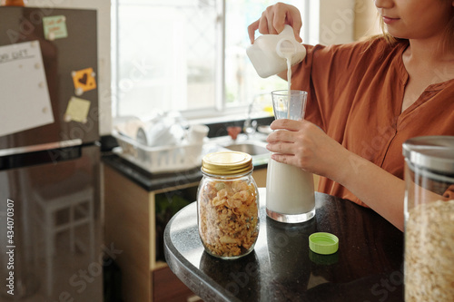 Cropped image of young woman filling glass jar with fresh whole milk