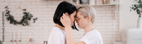 side view of young lesbian couple hugging in kitchen, banner © LIGHTFIELD STUDIOS