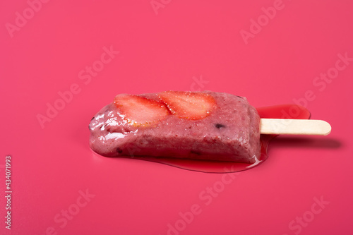 side view Brazil berry flavor popsicle with strawberry slices starts melting on a rose red background