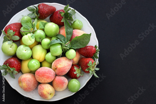 Top view of Fresh summer fruits  plum  peach  apricot  strawberry in plate on black background  copy space  food concept.