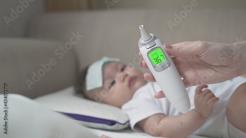asian woman mother using digital thermometer scan baby infant temperature for sickness and result no fever. parent routine checking up daughter health by medical equipment at home. baby get well cold.