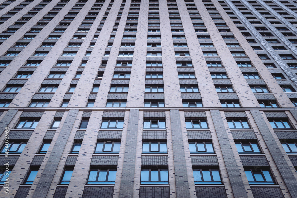 Facade of a huge modern residential skyscraper. Rows of windows. Monotonous colors in dark tones. Depressive urban environment. Lower angle view. Texture or background