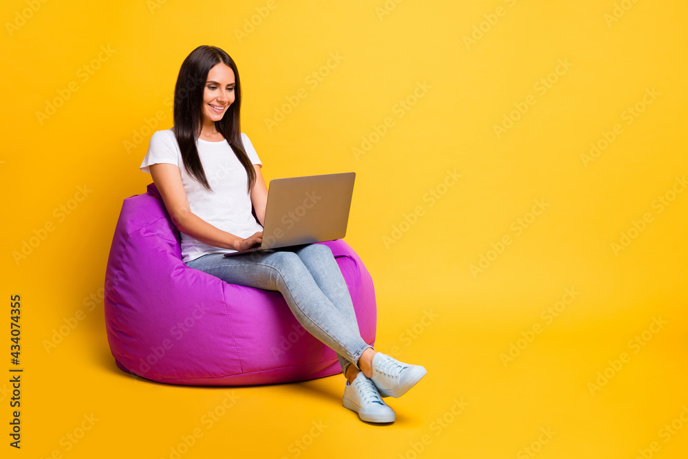 Full length body size photo pretty brunette working with computer programming in violet beanbag isolated on vibrant yellow color background Full length body size photo pretty brunette working with computer programming in violet beanbag isolated on vibrant yellow color background