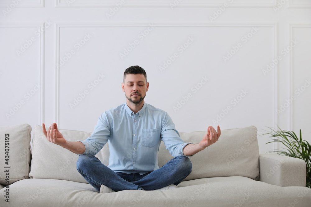 Man meditating on comfortable sofa in living room Man meditating on comfortable sofa in living room
