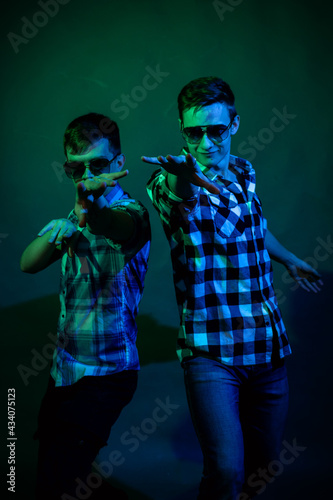 Two young men in plaid shirts dance in the studio with multicolored light