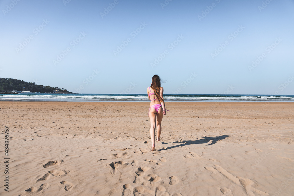 Young caucasian woman running to the sea on the beach with a pink bikini. Young caucasian woman running to the sea on the beach with a pink bikini.