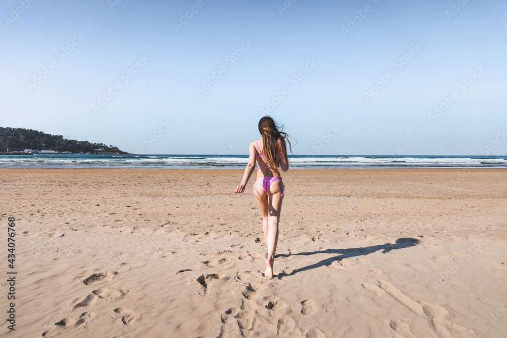 Young caucasian woman running to the sea on the beach with a pink bikini.