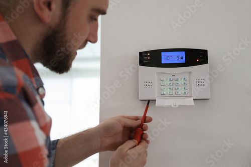 Man installing home security system on white wall in room, closeup