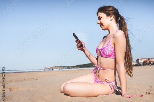 Young caucasian woman with a pink bikini on the beach using a mobile phone