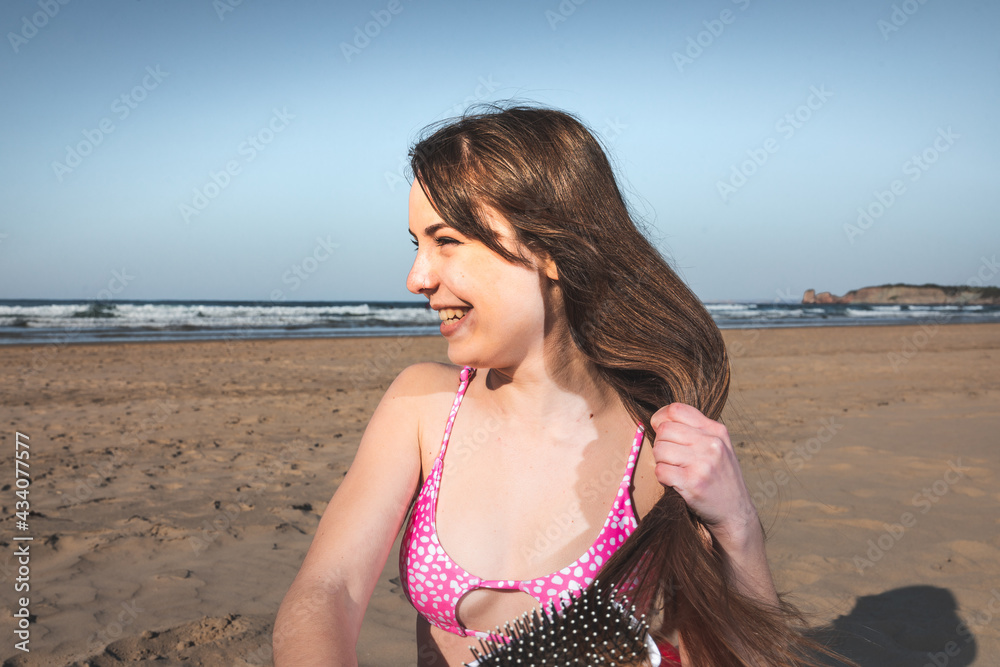 Young woman with a pink bikini on the beach brushing her hair with a comb.