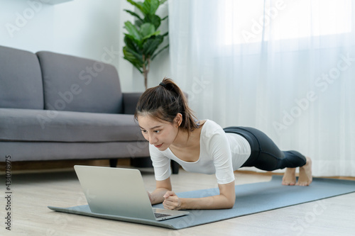 Fit, sporty asian young beautiful woman, girl doing yoga pose planking, watching trainer online on laptop computer, training in living room. Workout fitness exercise people in sportswear at home.