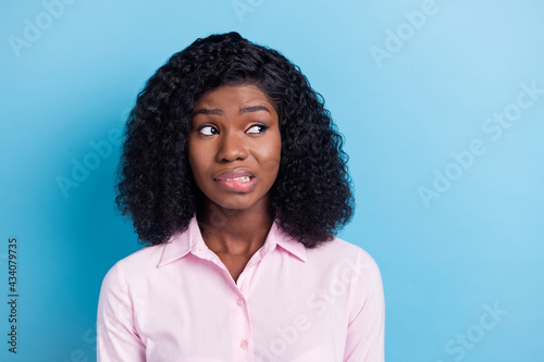 Photo of pretty doubtful dark skin woman wear pink outfit biting lip looking empty space isolated blue color background