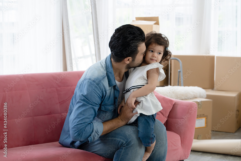 Caucasian family young father with beard kissing his little daughter at cheek while sitting together on sofa at new house Caucasian family young father with beard kissing his little daughter at cheek while sitting together on sofa at new house