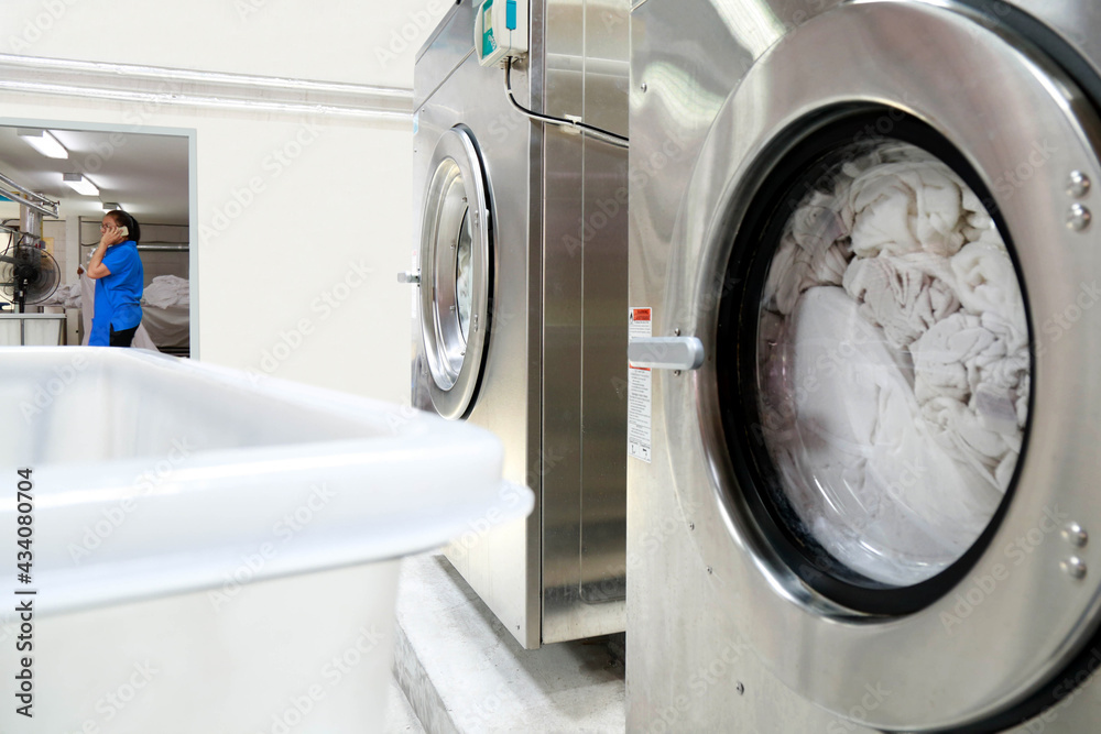 Industrial washing machine are spinning while a laundry staff is talking on the phone over the background. Shot taken in the factory. Industrial washing machine are spinning while a laundry staff is talking on the phone over the background. Shot taken in the factory.