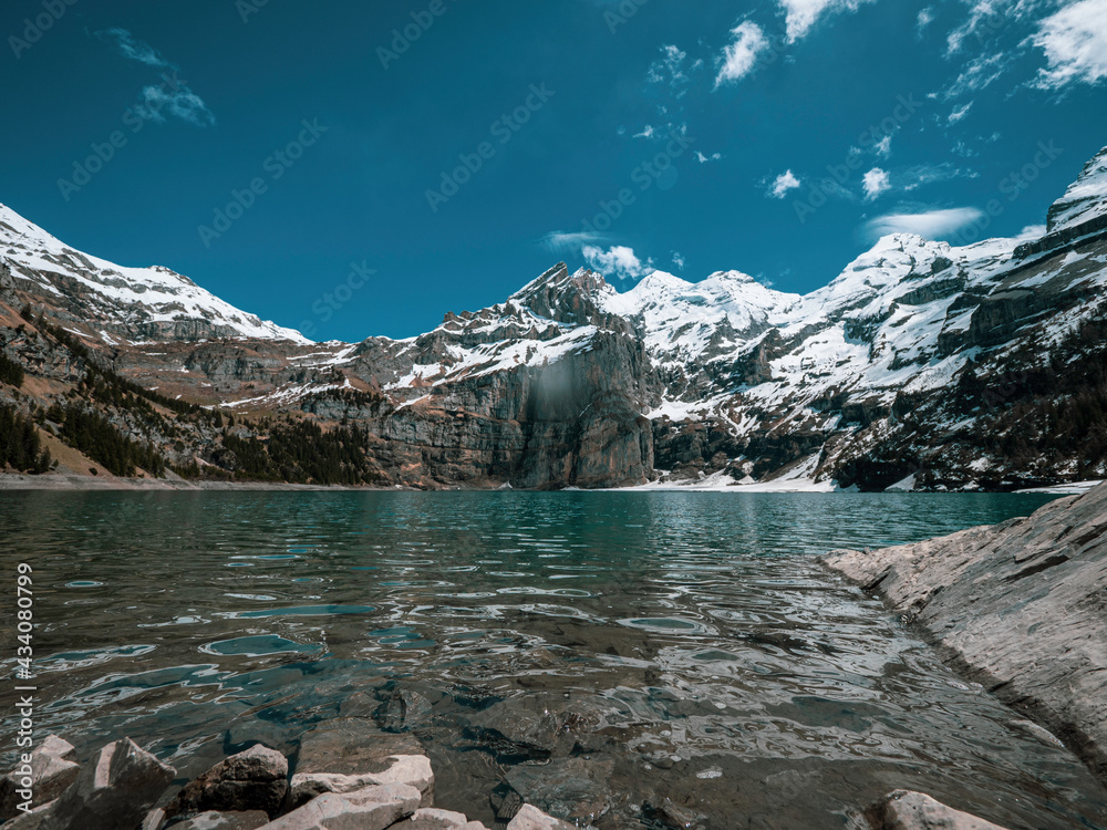 High alpine lake of Oeschinensee in Kandersteg, Switzerland. The picturesque clear blue lake is surrounded by high snow covered mountains, glaciers and pine forests.