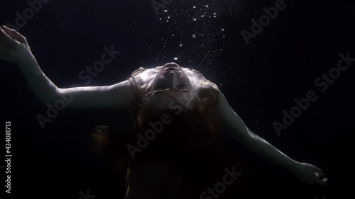 slowed down underwater portrait of woman facing the light floats up unconscious