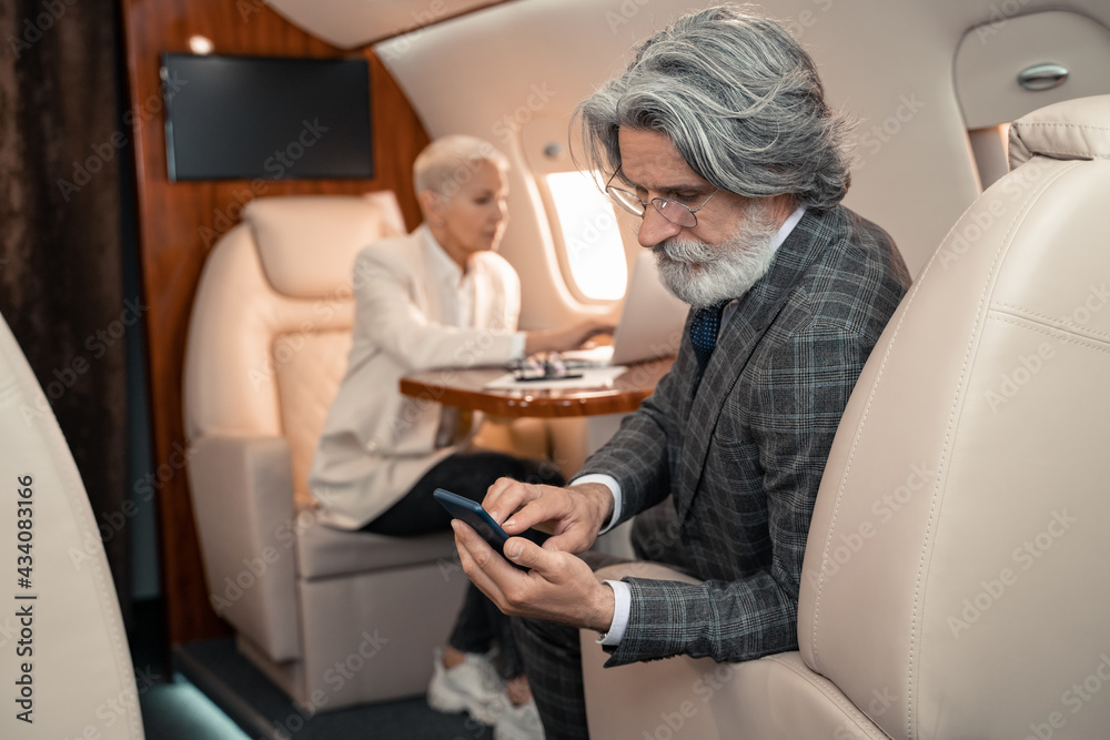 Businessman using smartphone near blurred businesswoman in plane Businessman using smartphone near blurred businesswoman in plane