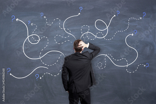 Right decision concept with man in black suit looking at chalkboard with painted dotted curved lines with question marks.