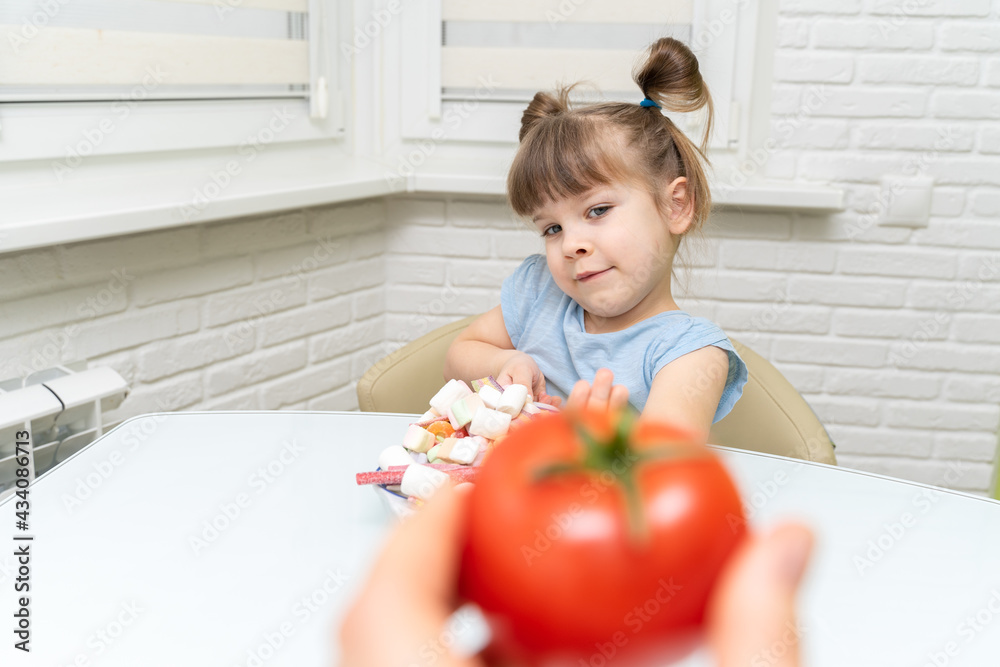 little girl makes a choice between candy and fruit. the child rejects healthy foods and chooses unhealthy foods little girl makes a choice between candy and fruit. the child rejects healthy foods and chooses unhealthy foods