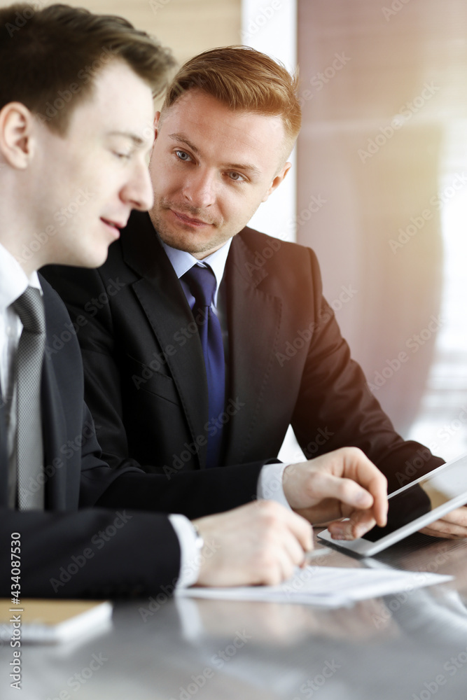 Businessman using tablet computer and work together with his colleague in sunny office. Unknown business people at meeting. Teamwork and partnership concept