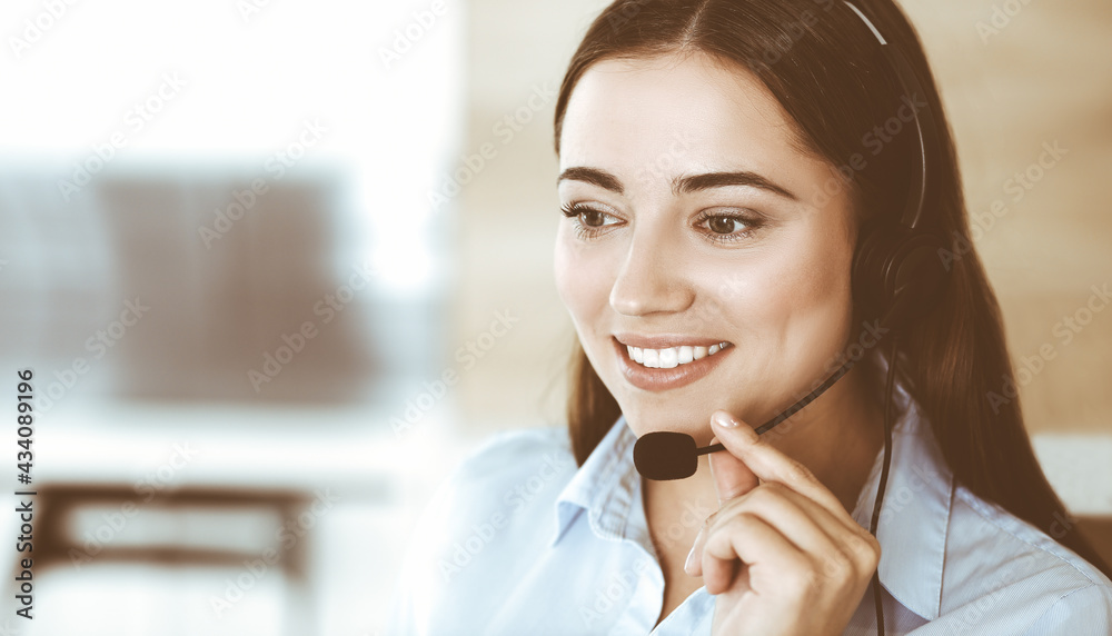 Brunette female customer service representative in a headset is consulting clients online. Call center and business people concept Brunette female customer service representative in a headset is consulting clients online. Call center and business people concept