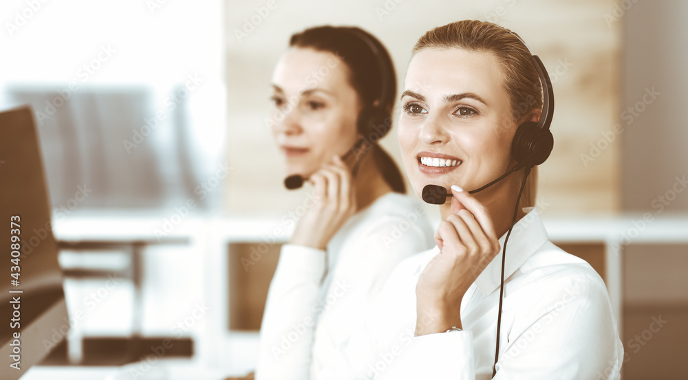Blond female customer service representative and her colleague are consulting clients online using headset. Call center and business people concept