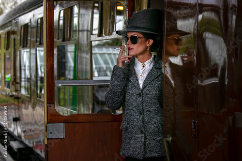 Fotografie Beautiful female in vintage 1920s costume smoking cigarette while leaving train
