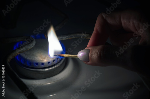 A burning matchstick in complete darkness ignites the natural gas of the home gas stove in the kitchen. Utilities concept.