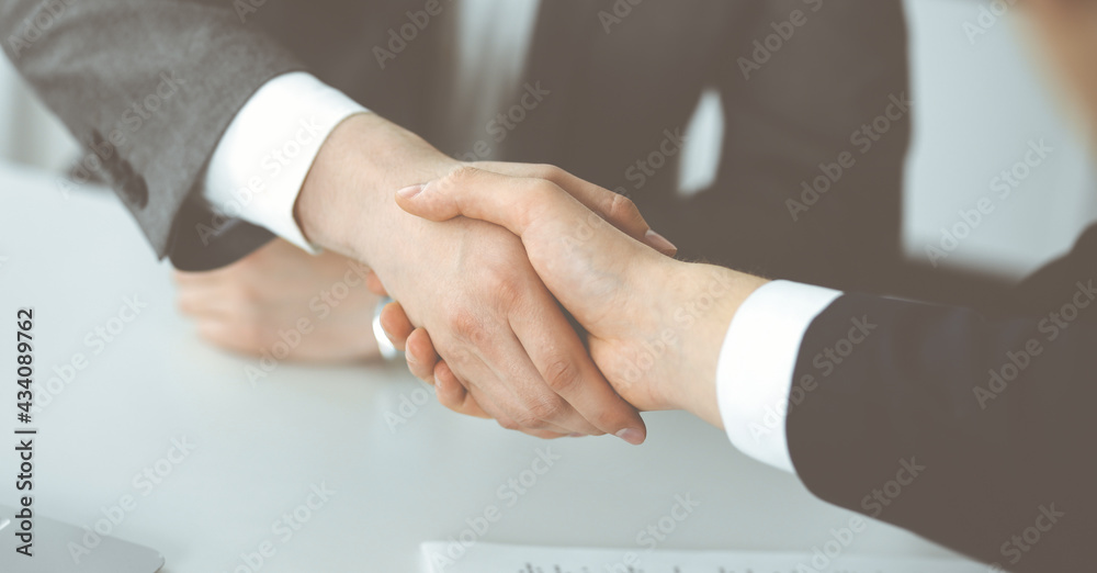 Unknown businessman shaking hands with his colleague or partner above the glass desk in modern office, close-up. Business people group at meeting
