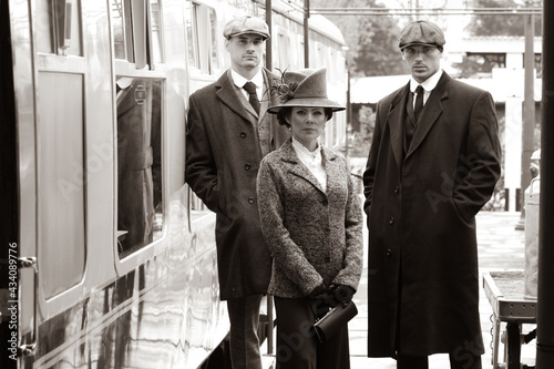 Gangster family of 1920s standing on railway station platform with train in the background