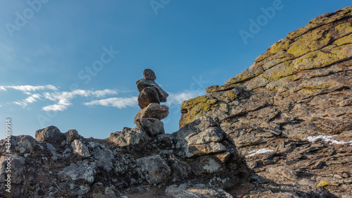 Granite rock, close-up. Yellow lichens grow on the cliff, cracks on the surface. A pyramid of stones stacked against a blue sky with white clouds. © Вера 