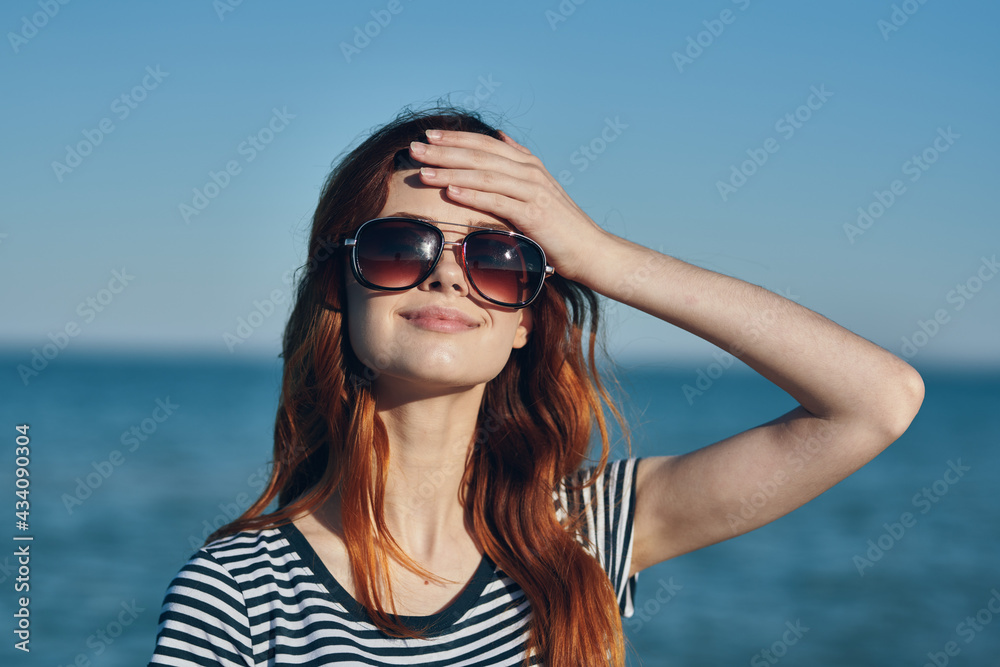 red-haired woman model in t-shirt and in sunglasses sea in the background summer vacation red-haired woman model in t-shirt and in sunglasses sea in the background summer vacation