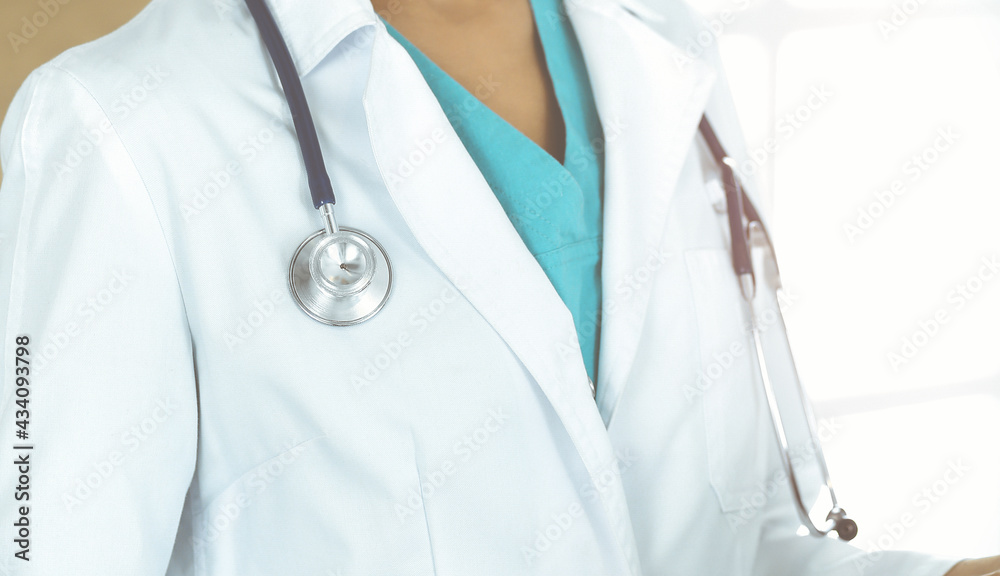 Unknown female doctor standing with stethoscope in sunny clinic, close-up Unknown female doctor standing with stethoscope in sunny clinic, close-up