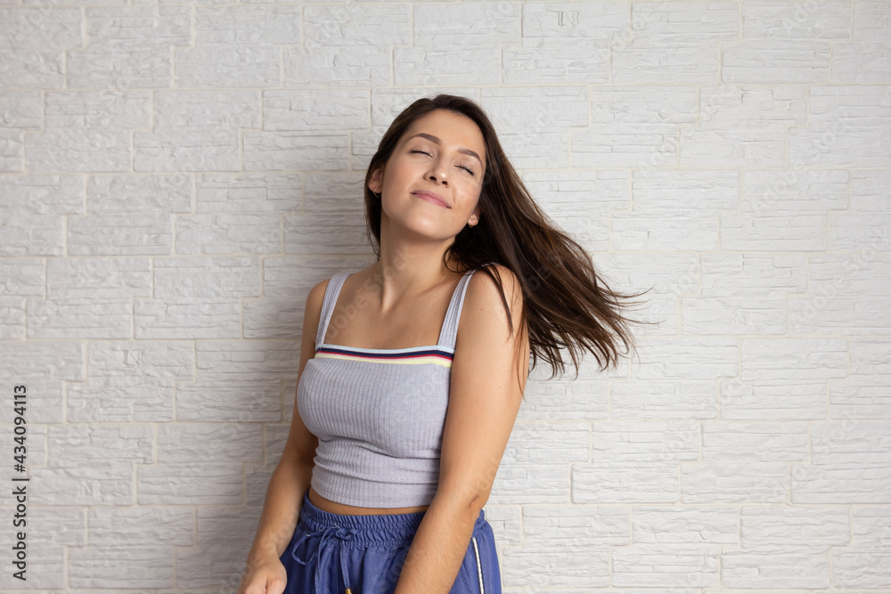 Portrait of happy pretty woman carefree and flipping hair. Eyes closed enjoying the moment. Isolated on white brick wall