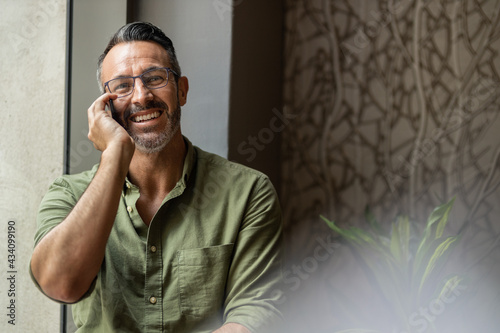 Smiling mature man with beard, glasses talking on phone, copy space photo