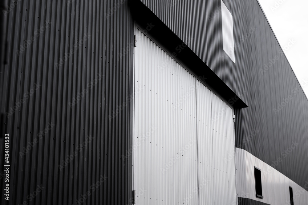 Black and white corrugated iron sheet used as a facade of a warehouse or factory with a windows. Texture of a seamless corrugated zinc sheet metal aluminum facade. Architecture. Metal texture. Black and white corrugated iron sheet used as a facade of a warehouse or factory with a windows. Texture of a seamless corrugated zinc sheet metal aluminum facade. Architecture. Metal texture.