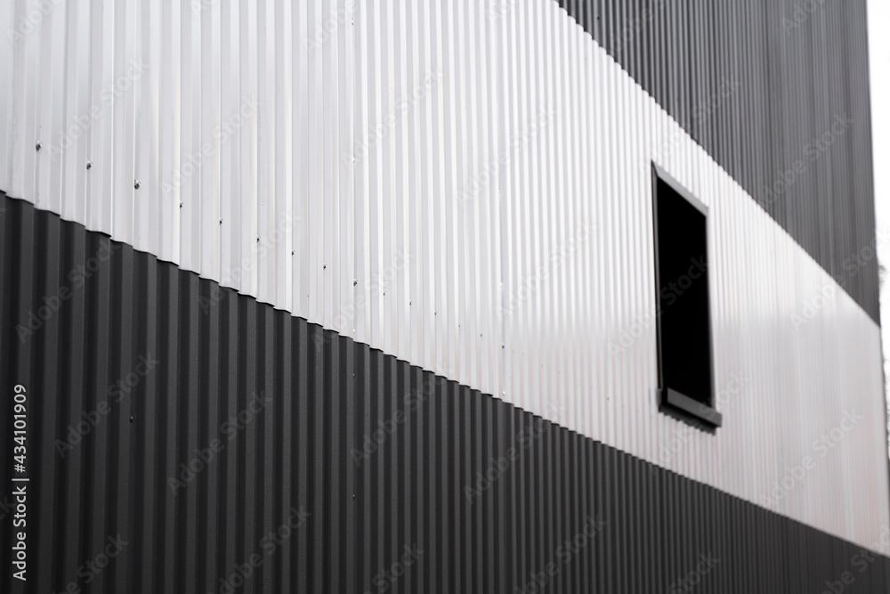Fototapeta premium Black and white corrugated iron sheet used as a facade of a warehouse or factory with a window. Texture of a seamless corrugated zinc sheet metal aluminum facade. Architecture. Metal texture.