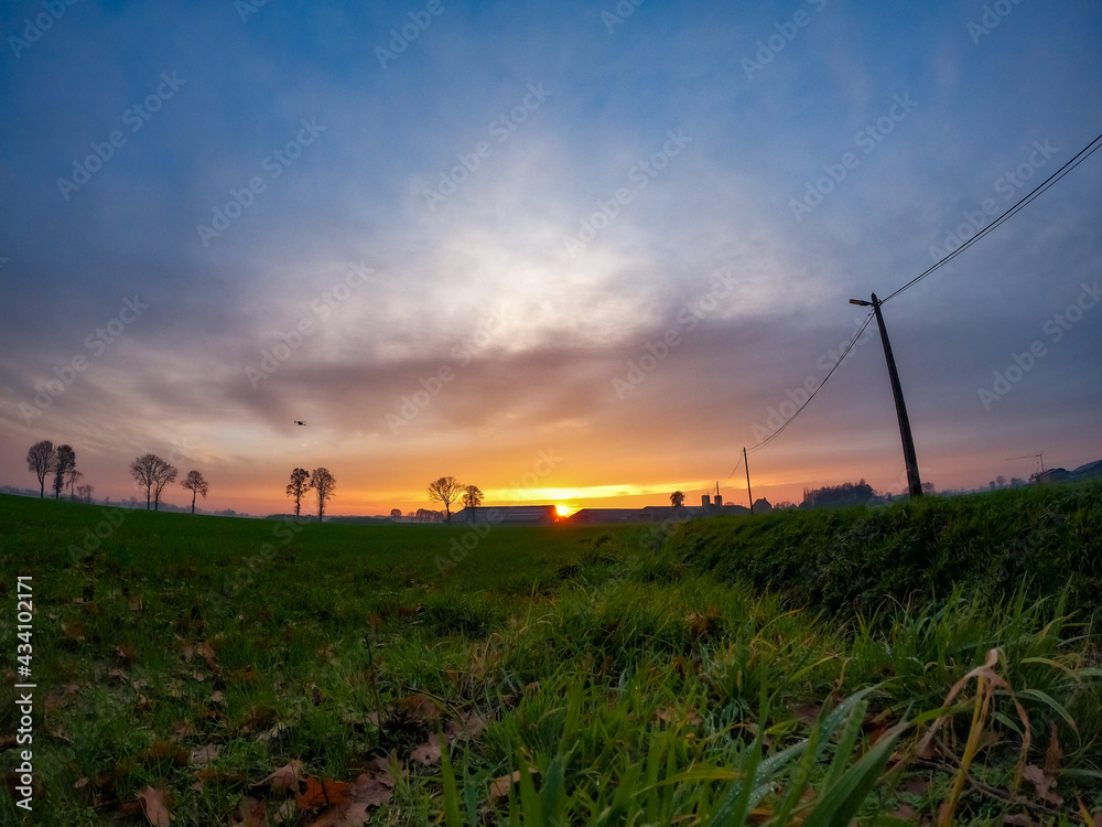 Dramatic and colorful Sunrise or sunset on a field covered with young green grass and yellow flowering dandelions in springtime. Sunbeams making their way through the clouds. High quality photo