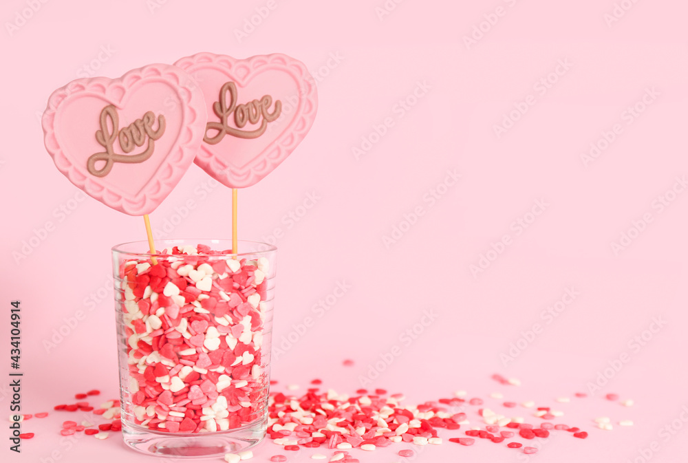 Chocolate heart shaped lollipops with word Love and sprinkles in glass on light pink background. Space for text