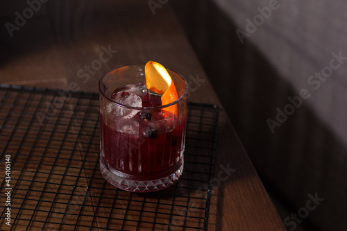 Alcoholic refreshing cocktail with black currants and decorated with orange in a transparent beautiful glass with ice on the table. Summer menu concept. Horizontal view